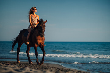 Gorgeous woman galloping on a horse on an ocean coast during a summer sunset