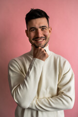 A man in a white sweater is smiling, holding his hand to his chin