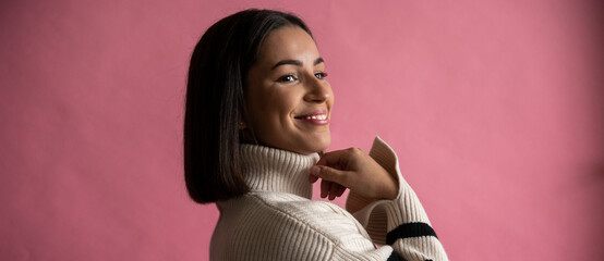 A happy woman in a white sweater smiles in front of a pink background