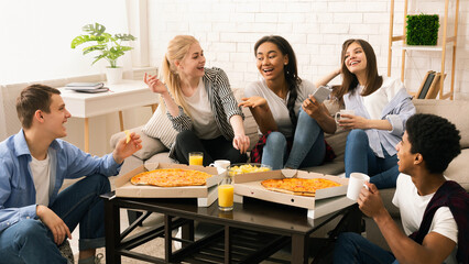 A diverse group of multiethnic friends are gathered around a wooden table. They are enjoying slices...