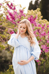 Fototapeta premium Pregnant woman 24-29 year old wearing linen dress over nature background with flowers outdoor. Motherhood. Springtime season.