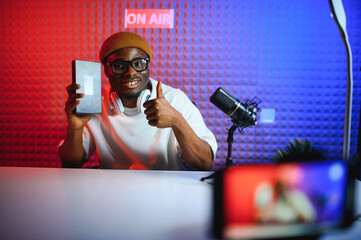 Young african american man recording or streaming podcast using microphone at his small broadcast...