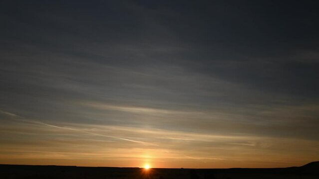 Time lapse of a colorful sunrise with the sun slowly rising above the horizon.  The midground is a flat treeless prairie with small hills.
