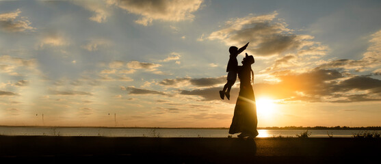 Silhouette of Asian Mother and Happy son greeting, proud and hug together with sunset background....