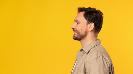 A man is standing upright in front of a bright yellow background. He is positioned centrally in the...