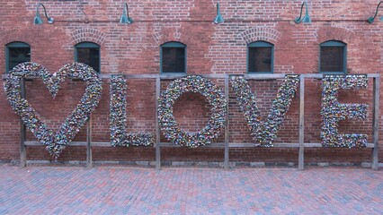 Naklejka premium Love letters made of locks at the distillery district in the city of Toronto Old Town is a great photo Opportunity in the city - TORONTO, CANADA - APRIL 15, 2024