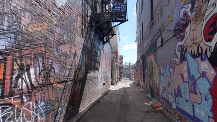Obraz premium Small and dirty alley with lots of graffiti at Kensington market in Toronto - TORONTO, ONTARIO - APRIL 15, 2024