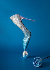 Elegant shoe made of glitter with a high heel on top standing on a silver egg. Minimal concept of...