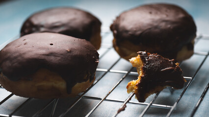 Chocolate donuts, with one half-eaten, placed on a cooling rack against a blue background. The image features selective focus.