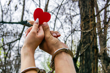 Two handcuffed hands are holding a red heart in the air, which suggests love, shyness and, possibly, a struggle for freedom or relationship difficulties.