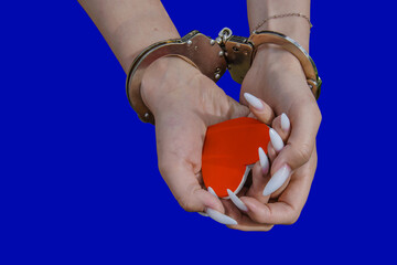 A pair of handcuffed hands gently hugs a bright red heart, creating a sharp contrast against a simple blue background. Themes of love, shyness, or the complexity of relationships.
