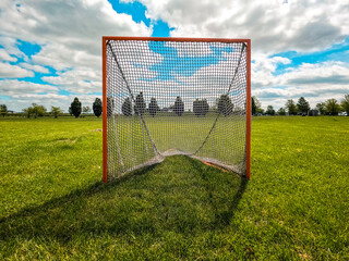 Sports Net in a Grassy Green Field. Front view of a lacrosse net set on a grassy green field. Park-like setting in the background of view with green leafy trees and a perfect cloudy summer sky above. © Sanya Kushak