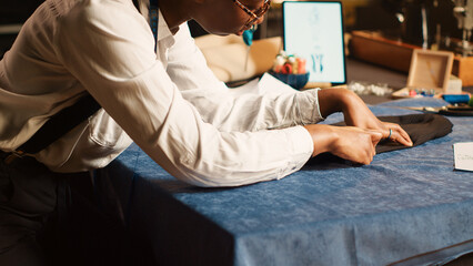 Seamstress preparing fabric on table, measuring material for right fit, custom made clothes. Couturier designing new fashion collection for luxury customers in atelier workshop. Handheld shot.