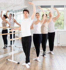 Motivated sporty young guy in white t-shirt and black sweatpants practicing balletic postures at...