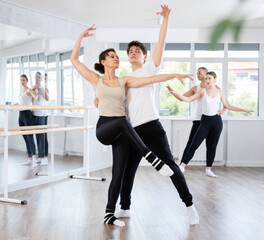 Focused graceful couple of ballet dancers showcasing skillful supports during group class in light-filled choreography studio