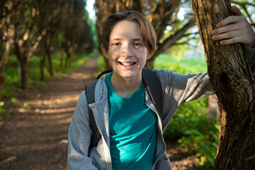 portrait of a smiling 11 year old boy with a backpack, near a tree in the park