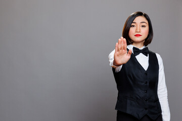 Serious asian waitress showing stop symbol with hand and looking at camera with confident face...
