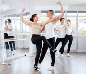 Confident concentrated man, ballet dancer, providing support of graceful female partner in challenging movements, during group rehearsal in vibrant choreography studio