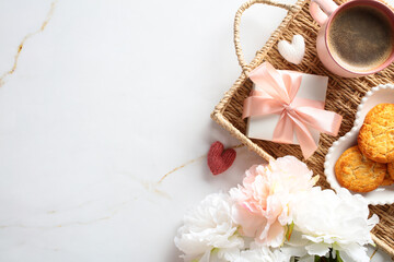 Wicker tray with gift box, coffee cup, cookies, bouquet of flowers on marble desk table. Happy Mother's Day concept. Top view.