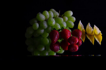 Still life with grapes, strawberries  and slice of lemon reflecting on black background