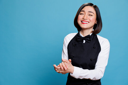 Smiling cafe waitress applauding with joy and encouragement, showcasing appreciation portrait. Attractive woman receptionist clapping hands and laughing while posing in studio - Powered by Adobe