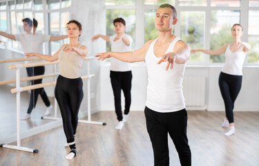 Experienced young male ballet dancer, dressed in white and black executing dance moves with focused...