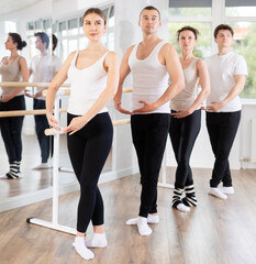 Dedicated female ballet dancer gracefully executing fifth position during group rehearsal in modern...