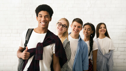Five cheerful teenagers, three girls and two boys, are seen lined up against a white brick wall...