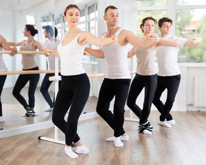 Group of men and women practicing plie ballet movement at barre in dance studio