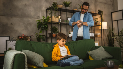 Father look at watch and wait son to finish his video game on tablet