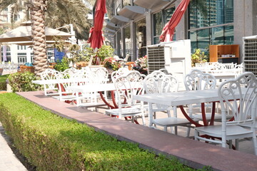 Summer terrace, outdoor city cafe, coffee house with white wooden tables, chairs and decorative street plants . Street drinks and snacks cafeteria