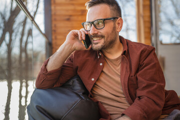 Portrait of adult man sit on the terrace and make a call on phone