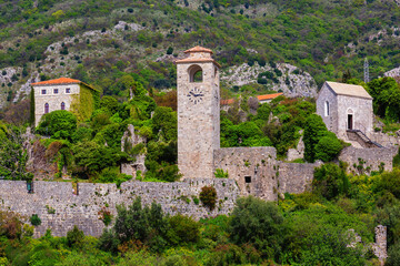 Fototapeta premium Historical ruins of Old Bar in Montenegro. Stone clock tower, ancient walls, and lush greenery, set against a mountain backdrop in spring. Travel and history themes