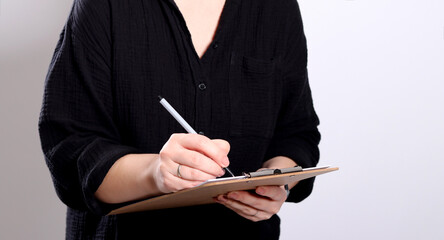 Close up of a blonde woman writing on a clipboard, grey empty studio background