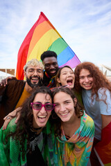 Diverse group of happy young people taking funny vertical selfie for social media celebrating gay...