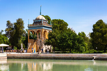 Bright and scenic view of the Emir's Summer Palace in Bukhara, featuring a vibrant pavilion by a reflective pond, surrounded by lush greenery and a clear blue sky. Bukhara, Uzbekistan - obrazy, fototapety, plakaty