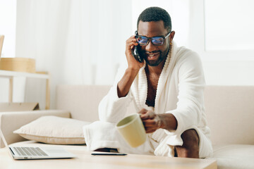Smiling African American Freelancer Working on Laptop in Modern Home Office, Talking on Phone in...
