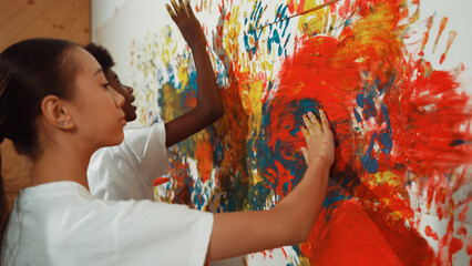 Diverse happy highschool girl and african boy paint the wall with water color in red and blue or...