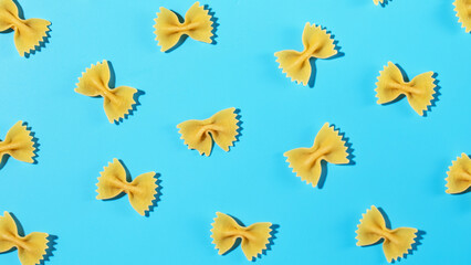 Uncooked bow tie pasta, farfalle scattered on a blue background in a decorative pattern