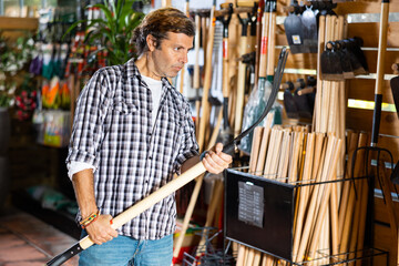 Experienced adult gardener choosing pitchfork in garden tools department of store ..