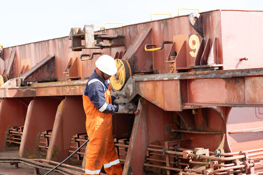 deck crew member of ship preparing hatch coaming surface plate uning pnumatic buffing grinder