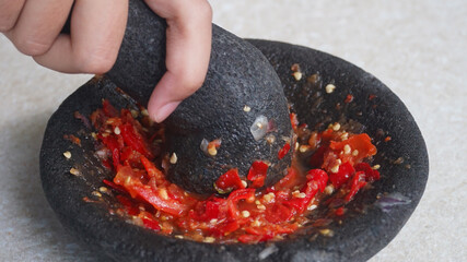 Chili and tomato sauce is being mashed on a stone mortar. Focus selected