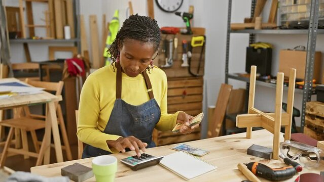 African woman calculating expenses with south african rands in a woodworking workshop indoors