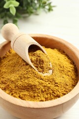 Dry curry powder in bowl and scoop on light table, closeup