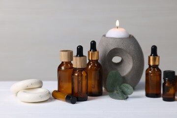 Different aromatherapy products, burning candle and eucalyptus leaves on white wooden table