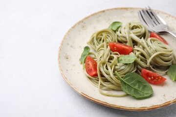 Tasty pasta with spinach, tomatoes and cutlery on light table, space for text