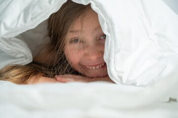 Portrait of a cute little girl laughing and hiding under the blanket. 
