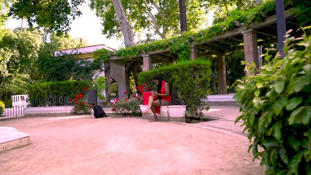 Mujer alegre sentada en un parque con una bebida refrescante revisando las compras que ha hecho en las tiendas y llamando a su amiga por el tel&eacute;fono m&oacute;vil.