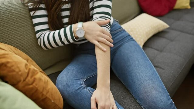 A young woman scratching her arm while sitting on a sofa in a cozy home setting, exuding a casual and domestic vibe.