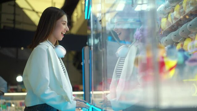 Happy young asian woman enjoy playing claw crane machine at game zone, people buying and shopping for relaxation at department store, concept of people lifestyle in urban.